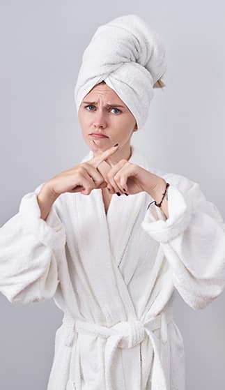 Image of a women in a white robe and a white towel wrapped around her hair with an annoyed look on her face and making an 'X' with her pointer fingers.