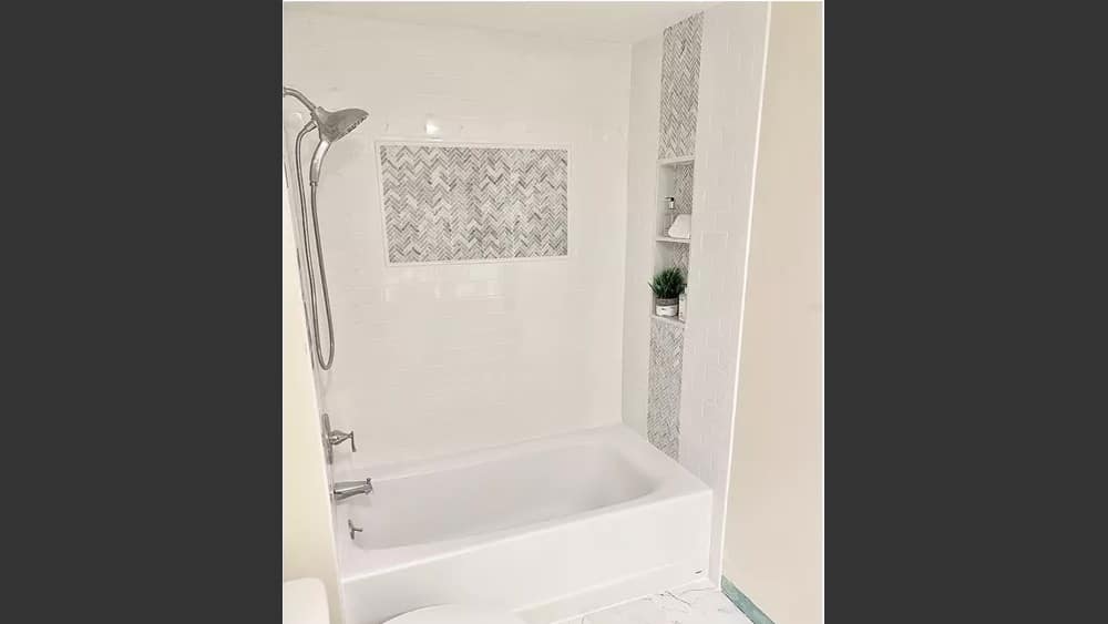 Image of toilet and tub/shower with beautiful Marble-like 12 by 12 floor tiles in white with grey veins on the floor and pearl white subway tiles on the shower walls with grey mosaic tile accents