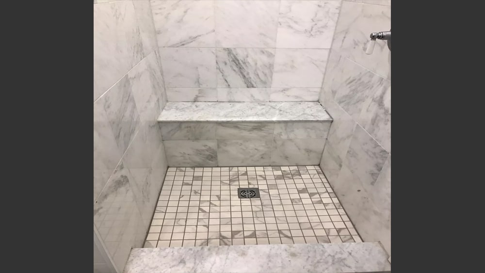 Image of shower stall with beautiful 12 by 12 inch white marble wall tiles with grey veins and a marble topped ledge for sitting.