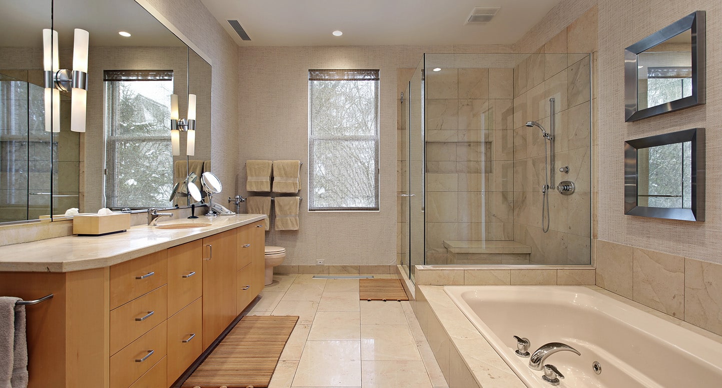 Image of a beautiful modern bathroom with subtle earthtone tiles, a light oak wood double vanity, a glass enclosed shower, and a floor level step-down spa-like tub.